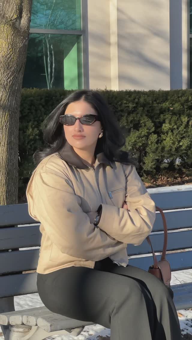 9 Trending Outfit Ideas for Women to Wear Right Now 6 Woman in beige jacket and black trousers sitting on a grey outdoor bench.