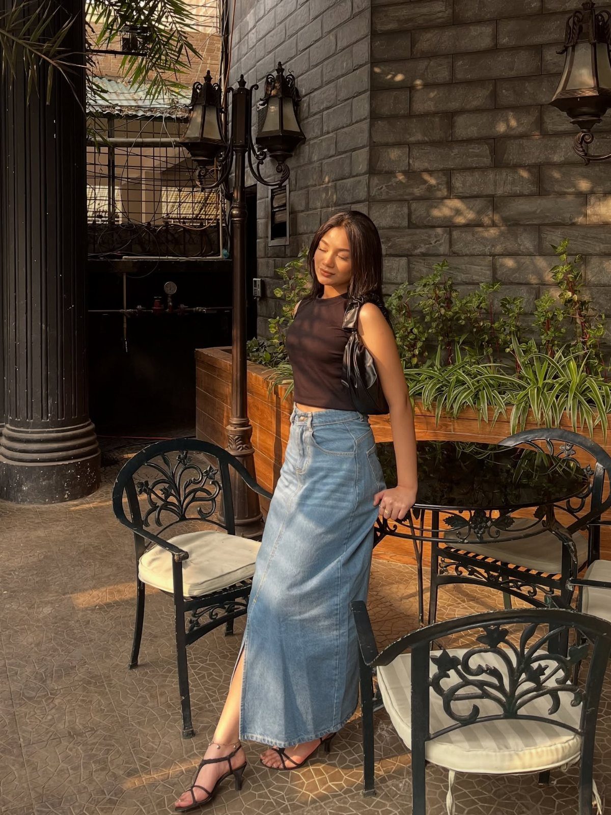 9 Trending Outfit Ideas for Women to Wear Right Now 2 Woman wearing a black sleeveless top and long denim maxi skirt at a cafe