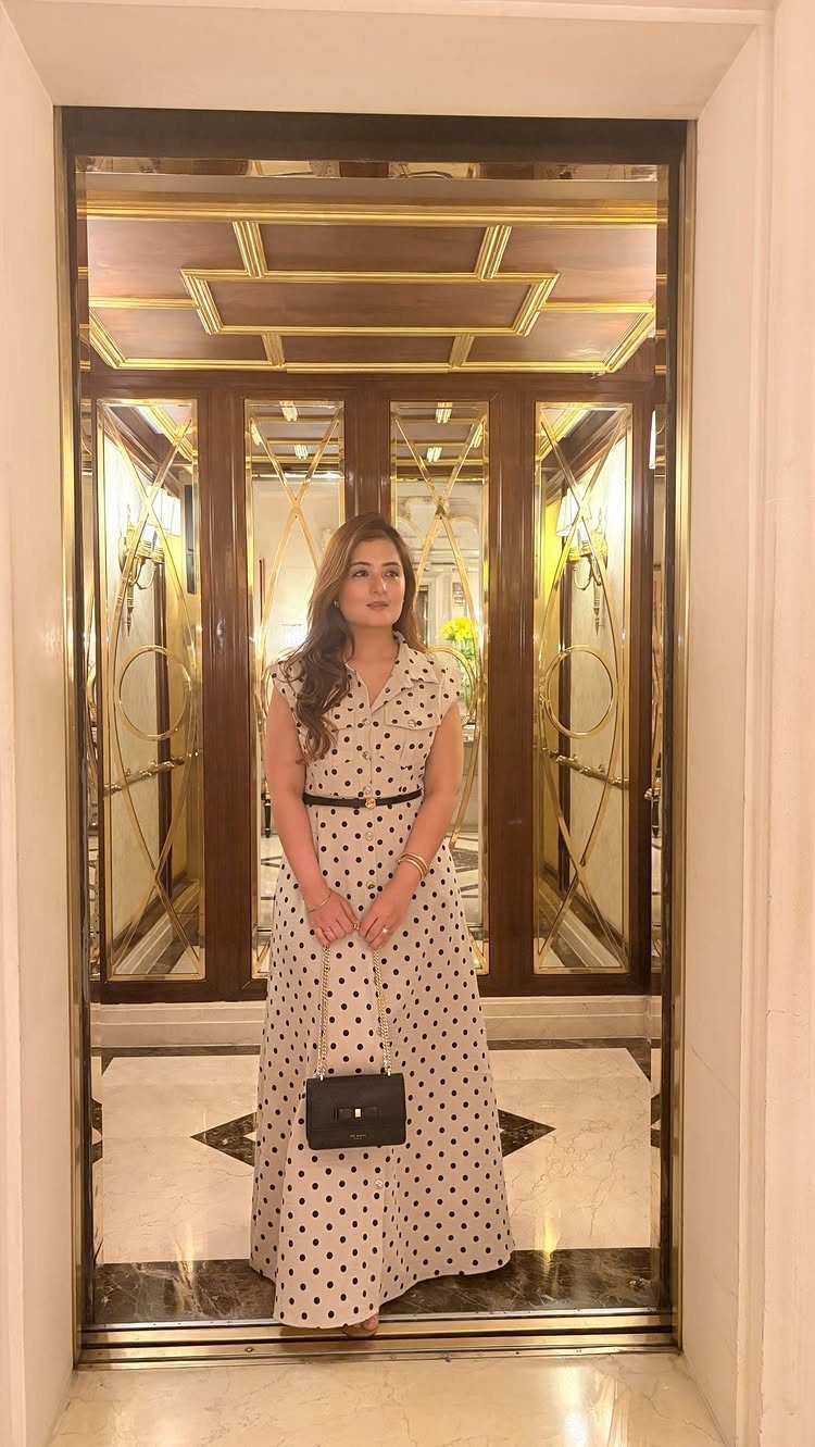 9 Trending Outfit Ideas for Women to Wear Right Now 7 Woman in a cream polka dot maxi dress with a black belt and handbag.
