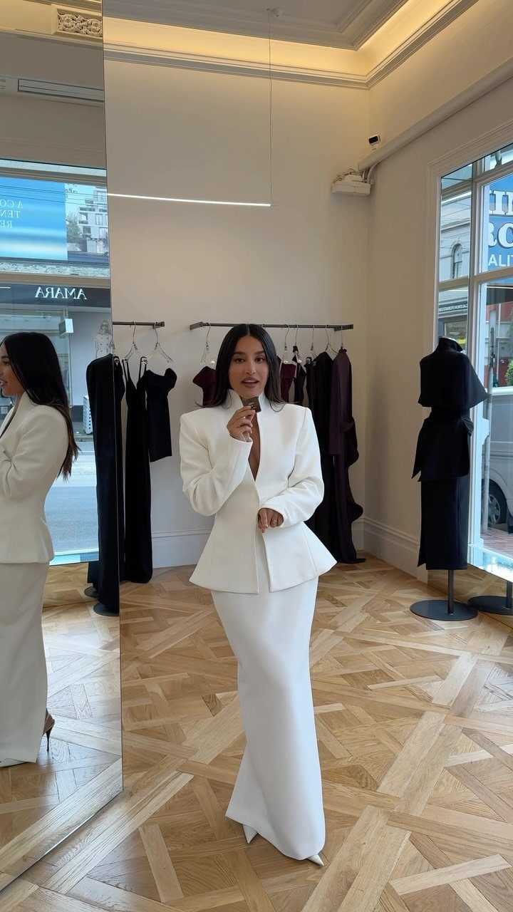 9 Trending Outfit Ideas for Women to Wear Right Now 1 Woman in a white tailored blazer and long skirt standing in a boutique.