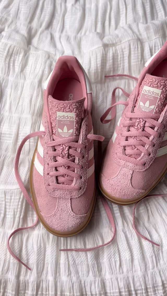 Pink suede adidas Samba sneakers with white stripes on white textured fabric.