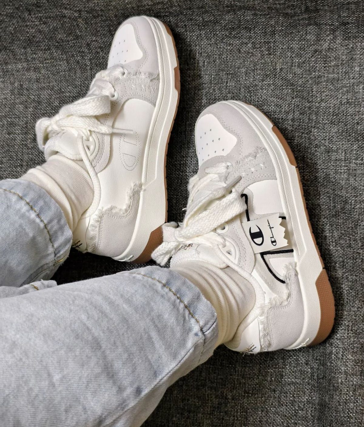 White chunky sneakers with frayed edges and gum soles worn with blue jeans.