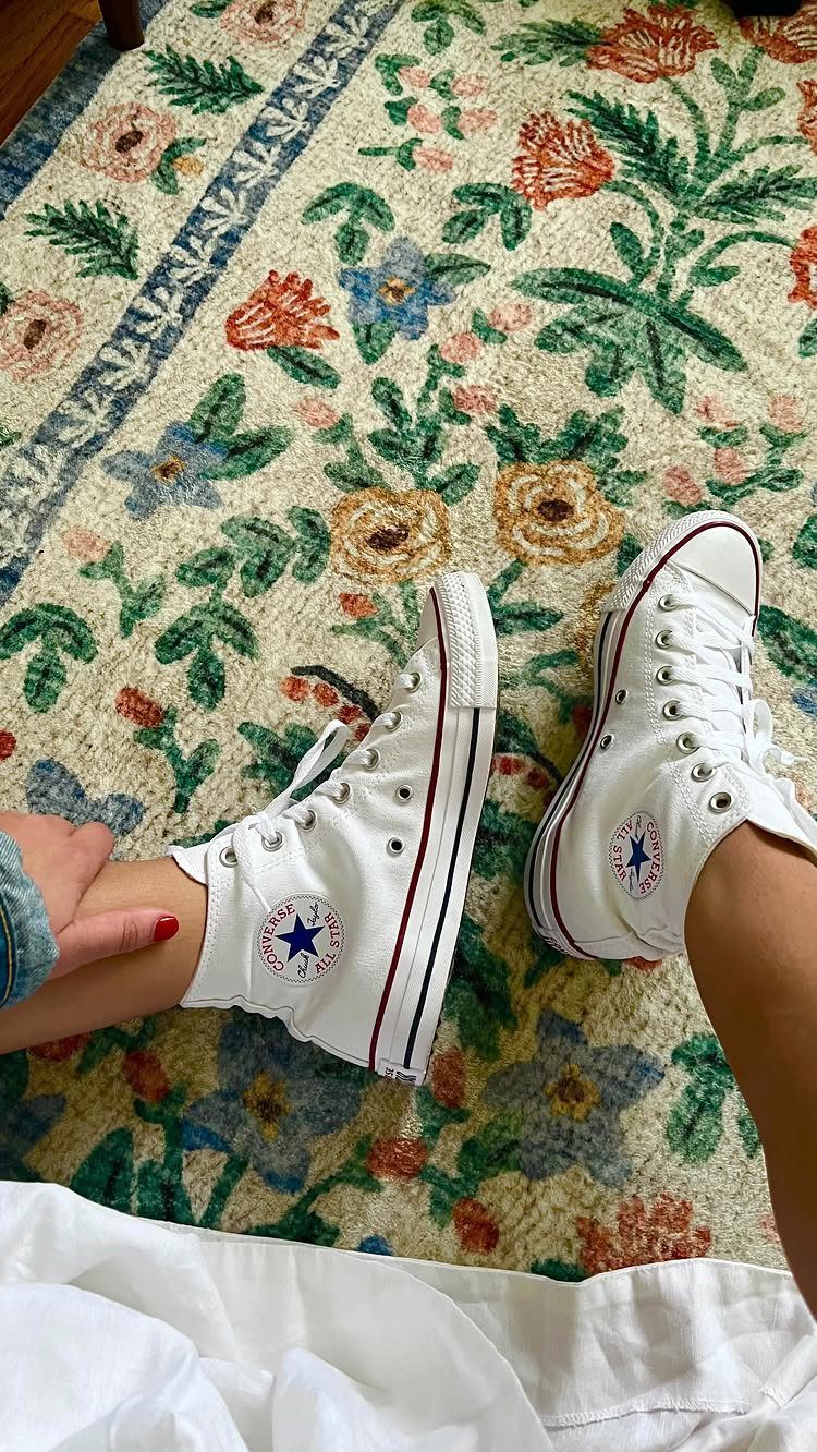 White high-top Converse sneakers on a colorful floral patterned rug.