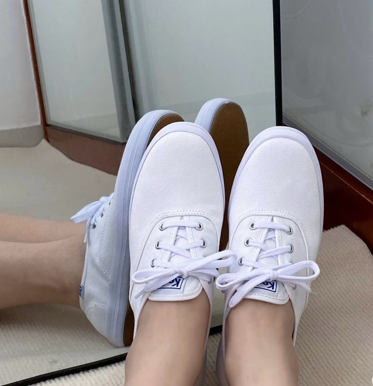 White canvas sneakers with white laces worn by a person near a mirror.