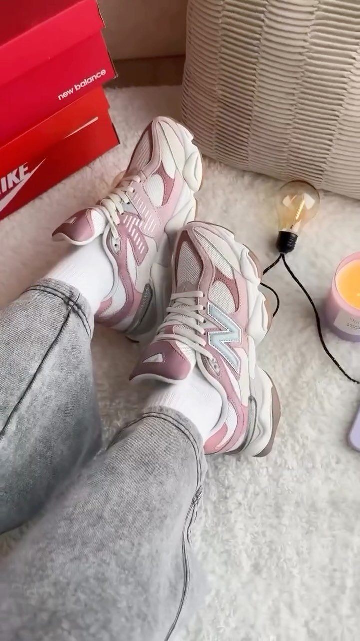 Pink and white New Balance 9060 sneakers worn with grey jeans on white rug.