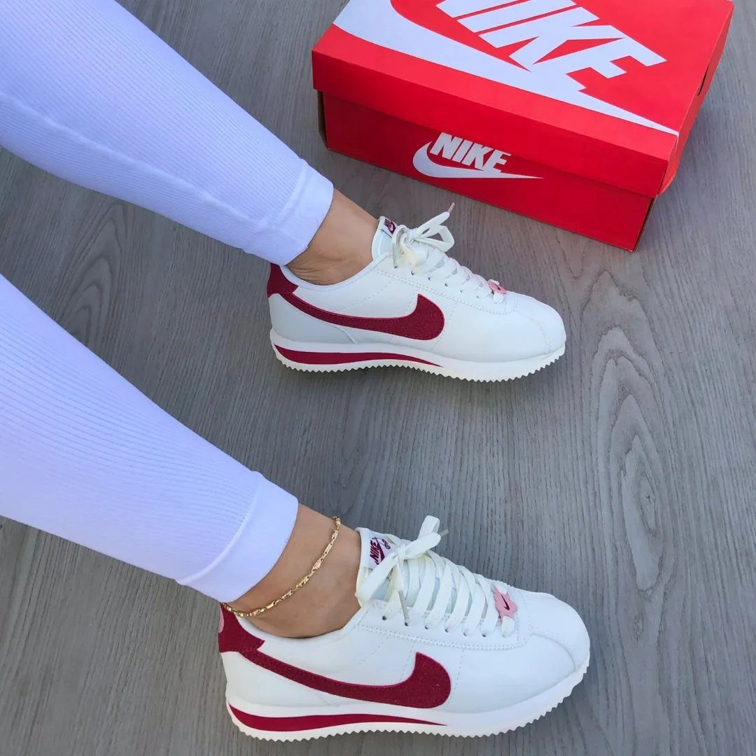 White Nike Cortez sneakers with burgundy accents worn with white leggings on wooden floor.