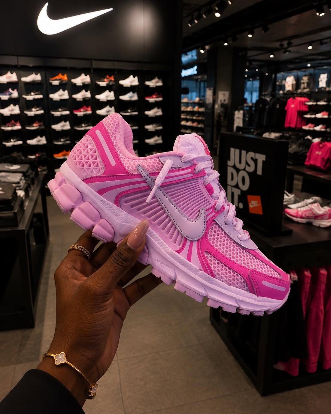 Pink and white Nike Zoom Vomero 5 sneaker held in a retail store.