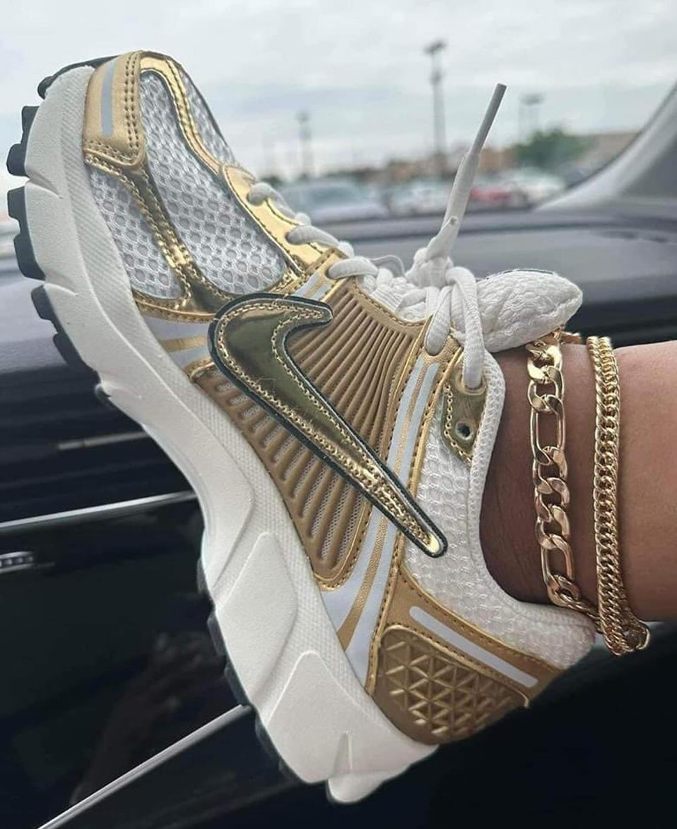 White and gold Nike sneaker with metallic accents and a gold chain bracelet.