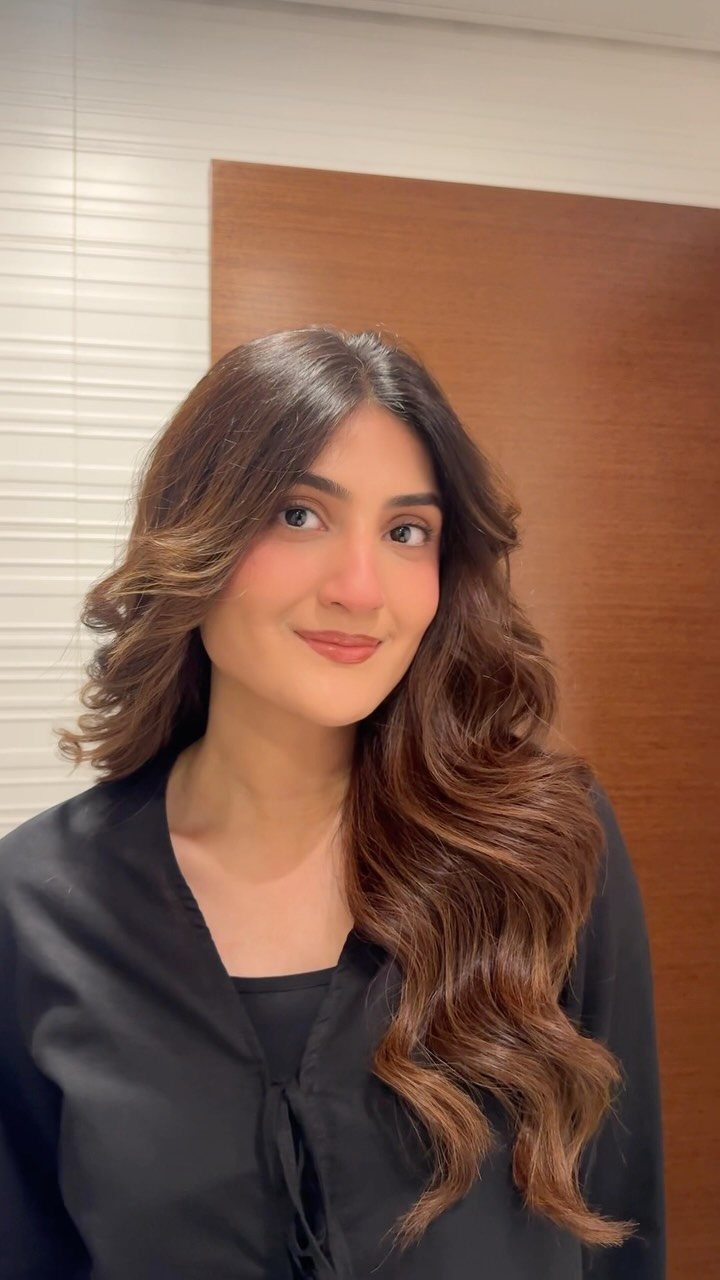 Wavy Hair Styles for Women: 12 Cuts and Looks to Try 6 Woman with long brown hair styled in center-parted beachy waves wearing black clothing