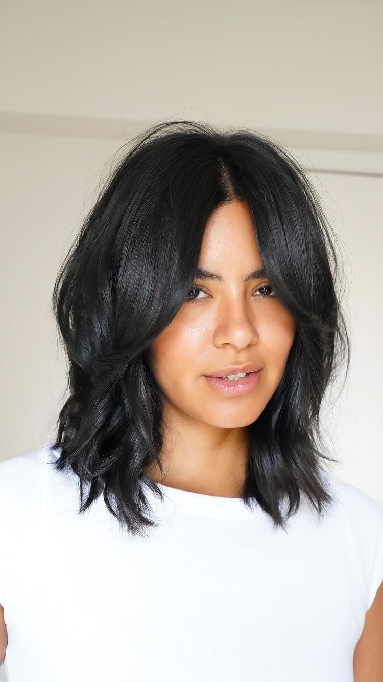 Wavy Hair Styles for Women: 12 Cuts and Looks to Try 3 Woman with a wavy black lob and curtain bangs wearing a white shirt.