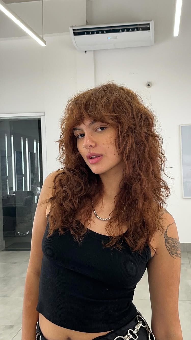 Wavy Hair Styles for Women: 12 Cuts and Looks to Try 4 Woman with shoulder-length reddish-brown wavy hair and curtain bangs wearing a black top.