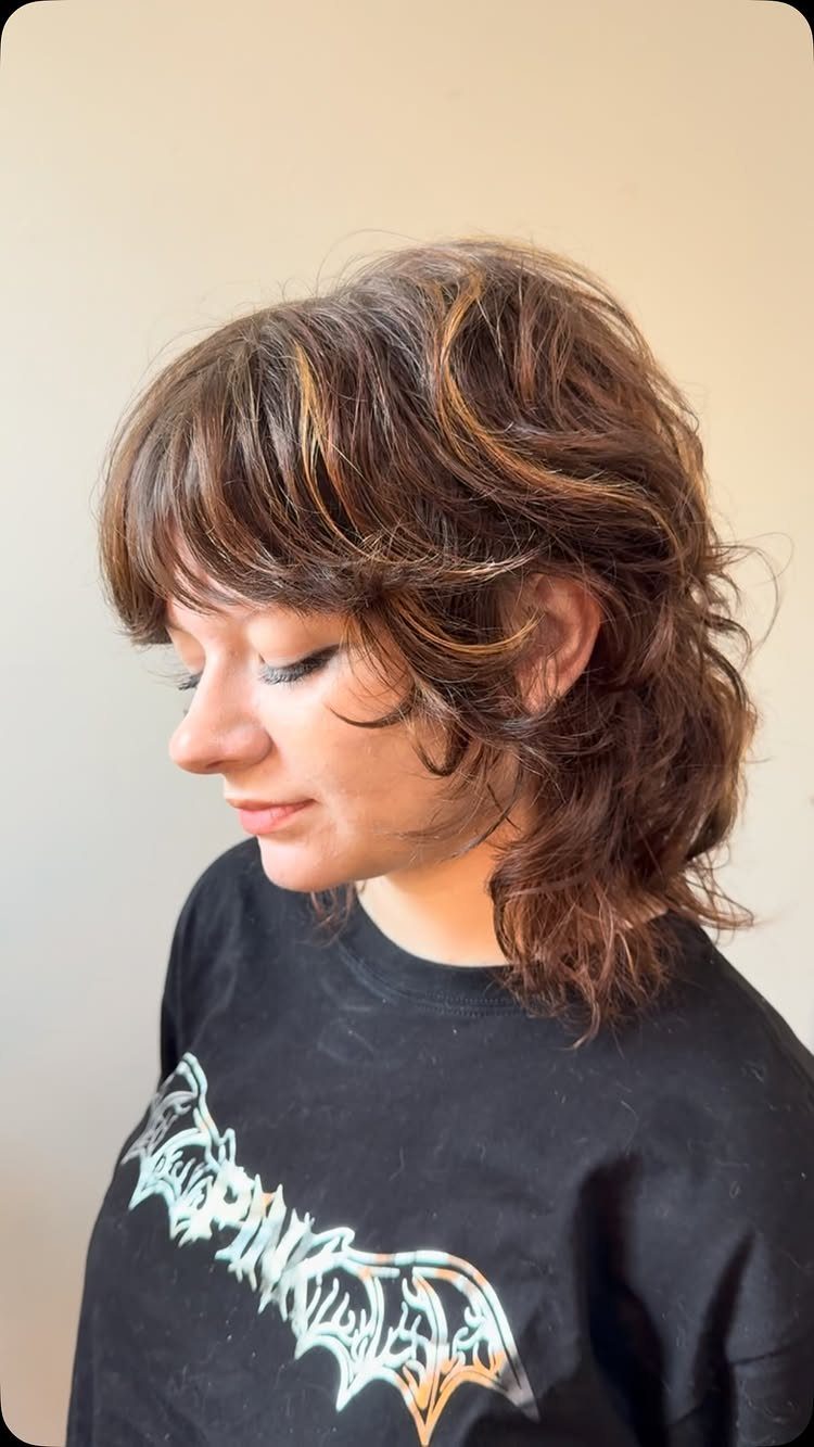 Wavy Hair Styles for Women: 12 Cuts and Looks to Try 8 Woman with a brown wavy wolf cut hairstyle and bangs wearing a black shirt.