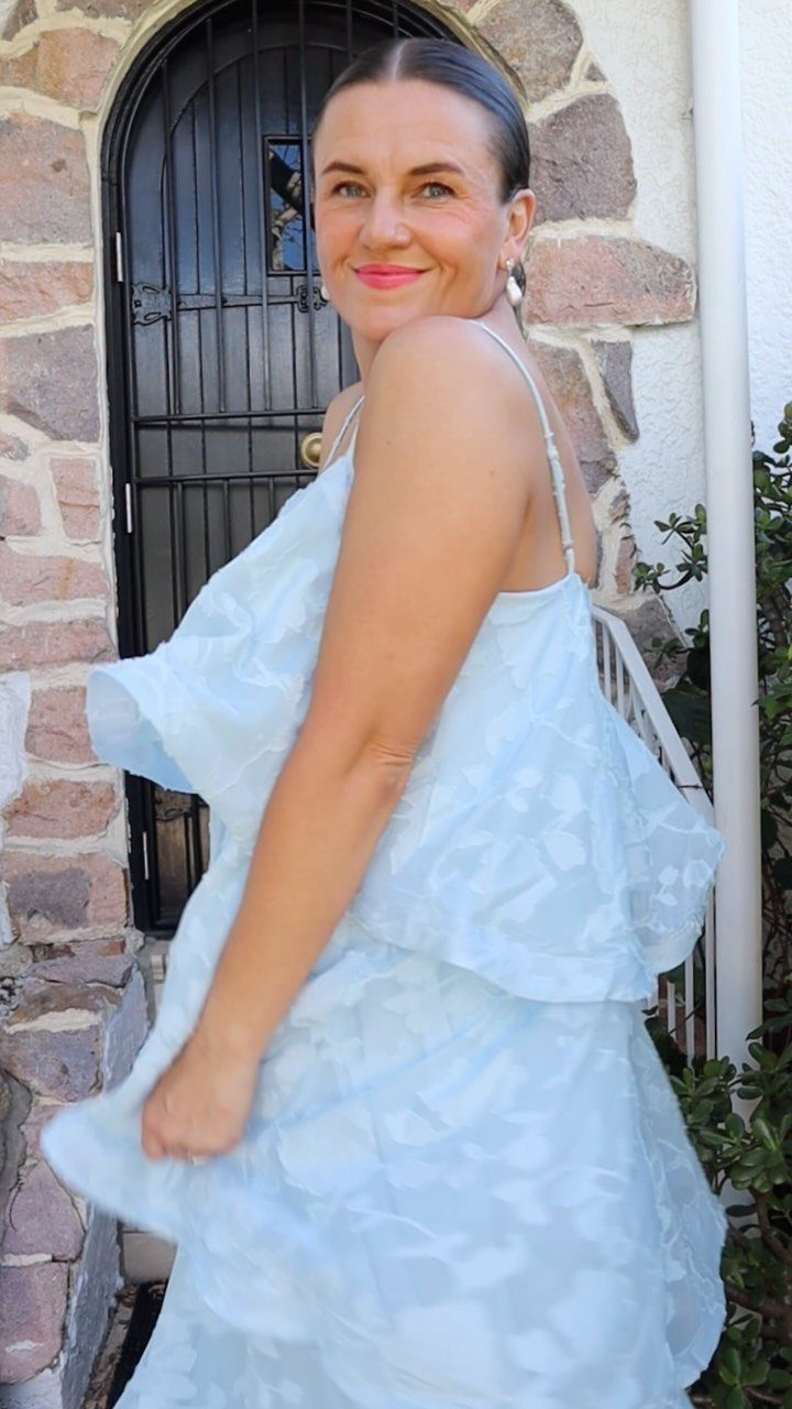 10 Wedding After Party Outfit Ideas for Guests 4 Woman in a light blue textured cocktail dress posing by a stone wall.