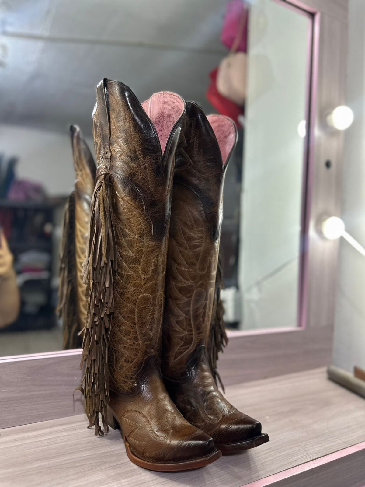 Western Dress Up: 5 Ideas, From Dresses to Denim Jackets 2 Brown leather cowboy boots with fringe standing on a wooden vanity table.