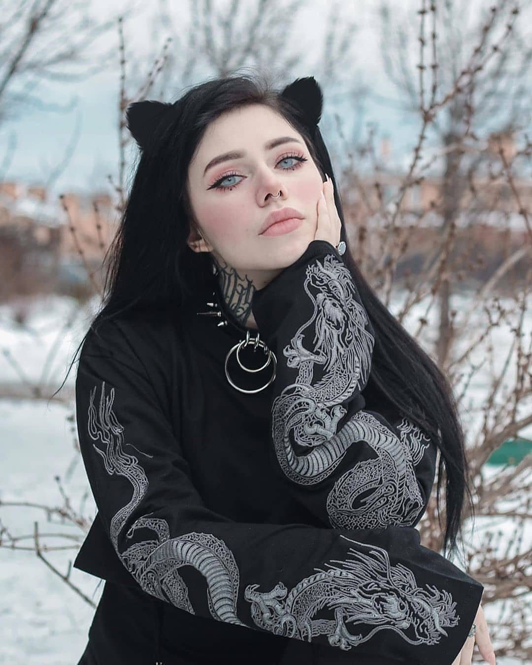 Woman in black dragon embroidered long-sleeved shirt posing in a snowy winter landscape.