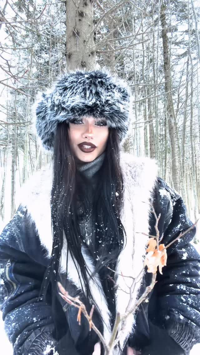 Person in winter goth attire with faux-fur hat and coat in snowy woods