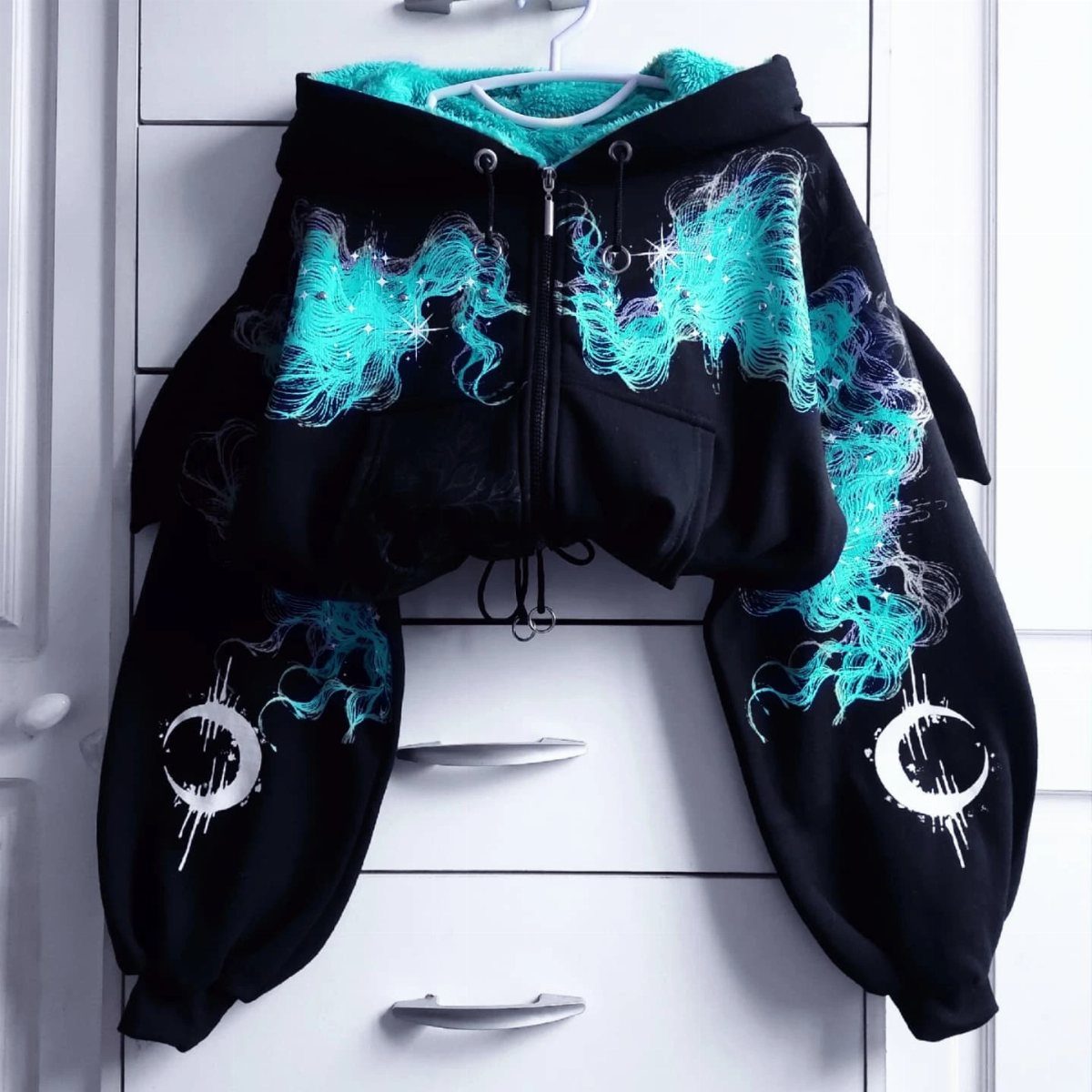 Black cropped hoodie with teal flame graphics and white crescent moons on sleeves.
