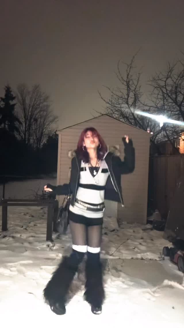 Person in goth winter attire standing in snow at night by a shed