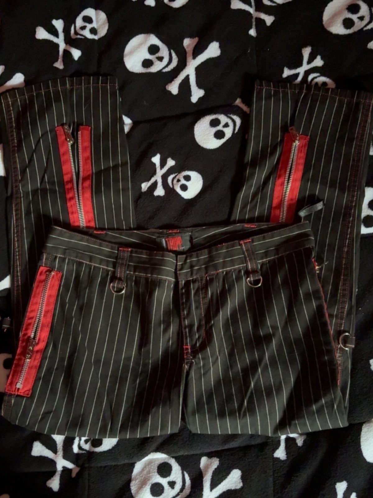 Black pinstriped pants with red zippers on a skull print background